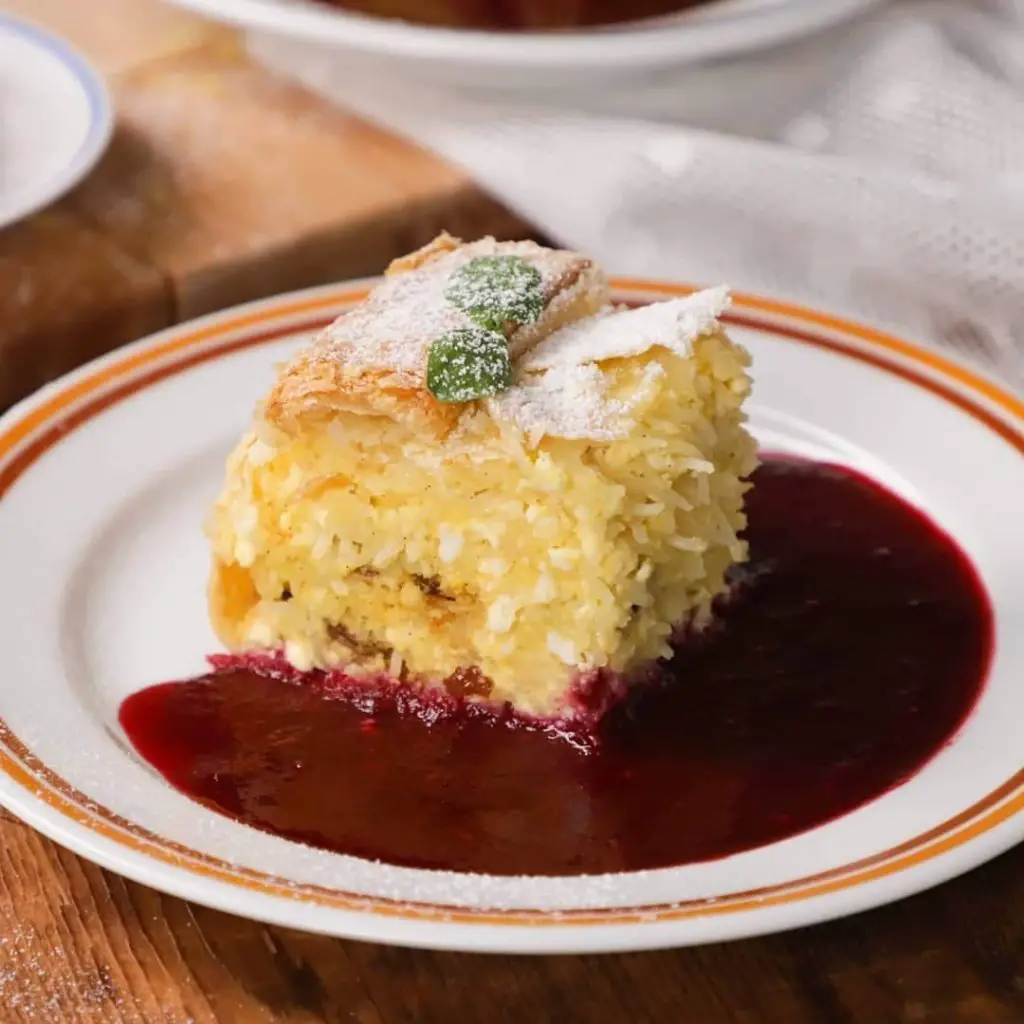 Vargabeles, a sort of noodle pie that is a traditional Transylvanian dessert (Hungarian/Romanian) on a plate with a berry sauce and powdered sugar.