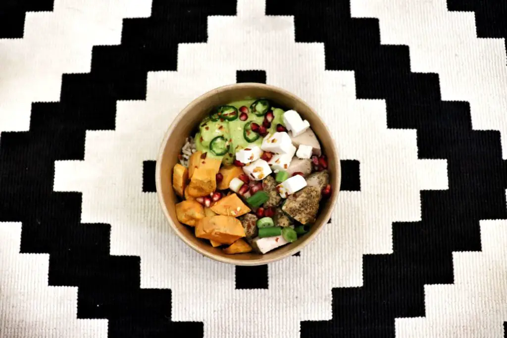 Vegetarian bowl of veggies, tofu, and jalapenos on a black and white table cloth.