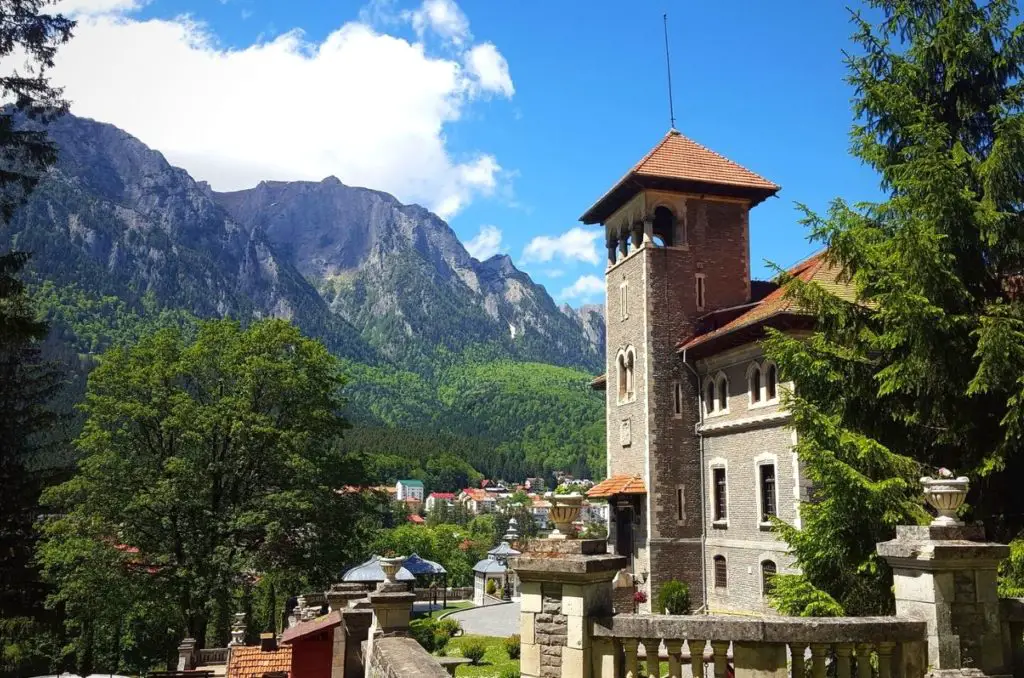 Cantacuzino Castle in Transylvania with mountains and clouds in the background.