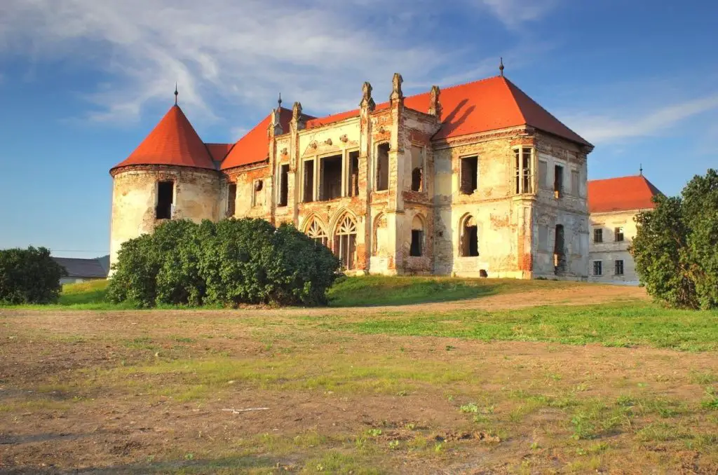 Banffy Castle in Transylvania, Romania with red roofs, green grass, and blue skies.