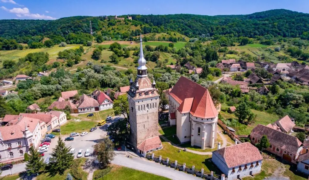 Fortified church of Saschiz from an aerial perspective with green trees and blue skies in the background.