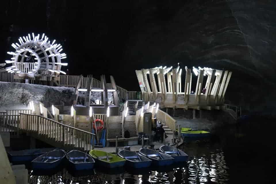 Underground amusement park in Turda Salt Mine with blue and yellow paddle boats docked on an underground lake.