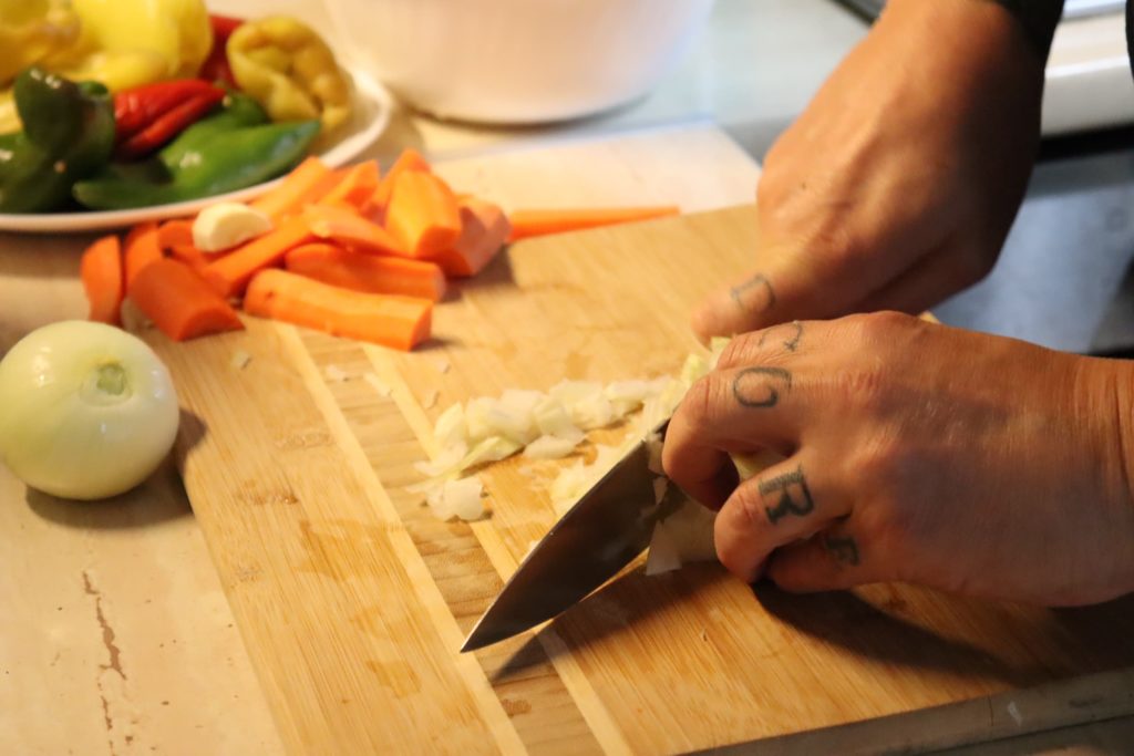 tattooed hands chopping onions on wooden cutting board