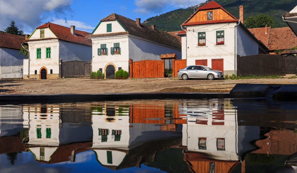 White houses in Rimetea Village reflecting in water with deep blue sky.