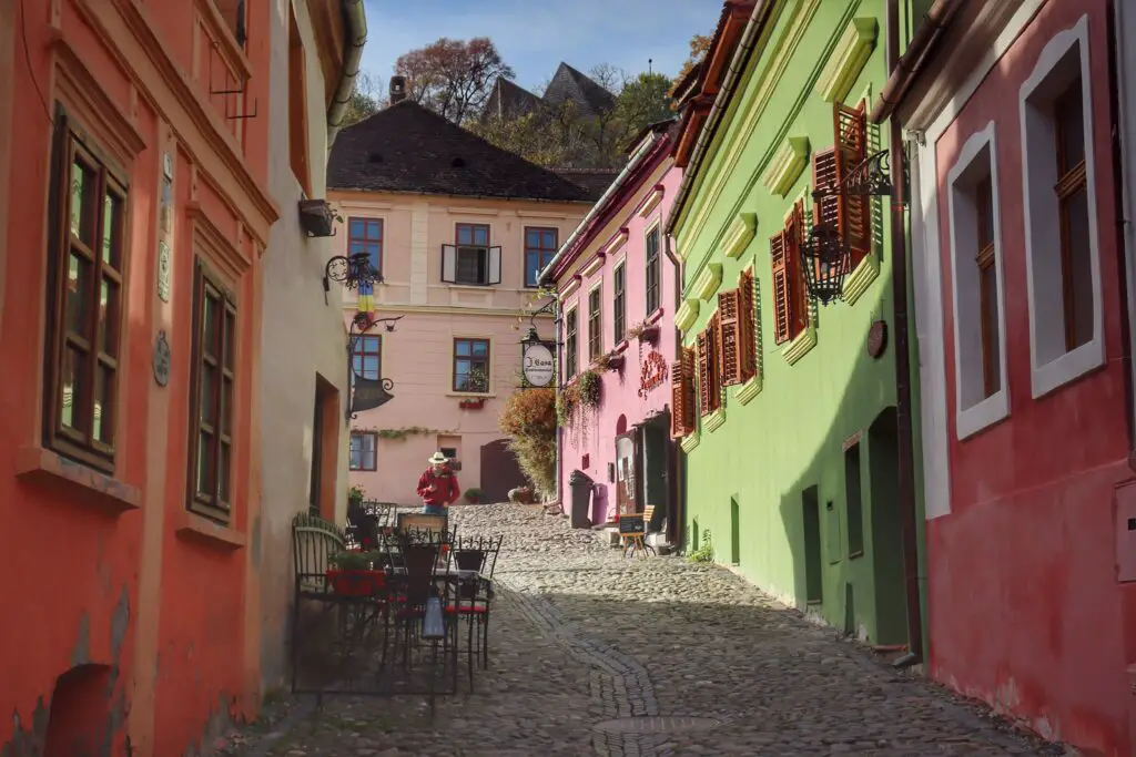 Hilly cobblestone street lined with colorful houses during golden hour in Sighisoara, Romania.