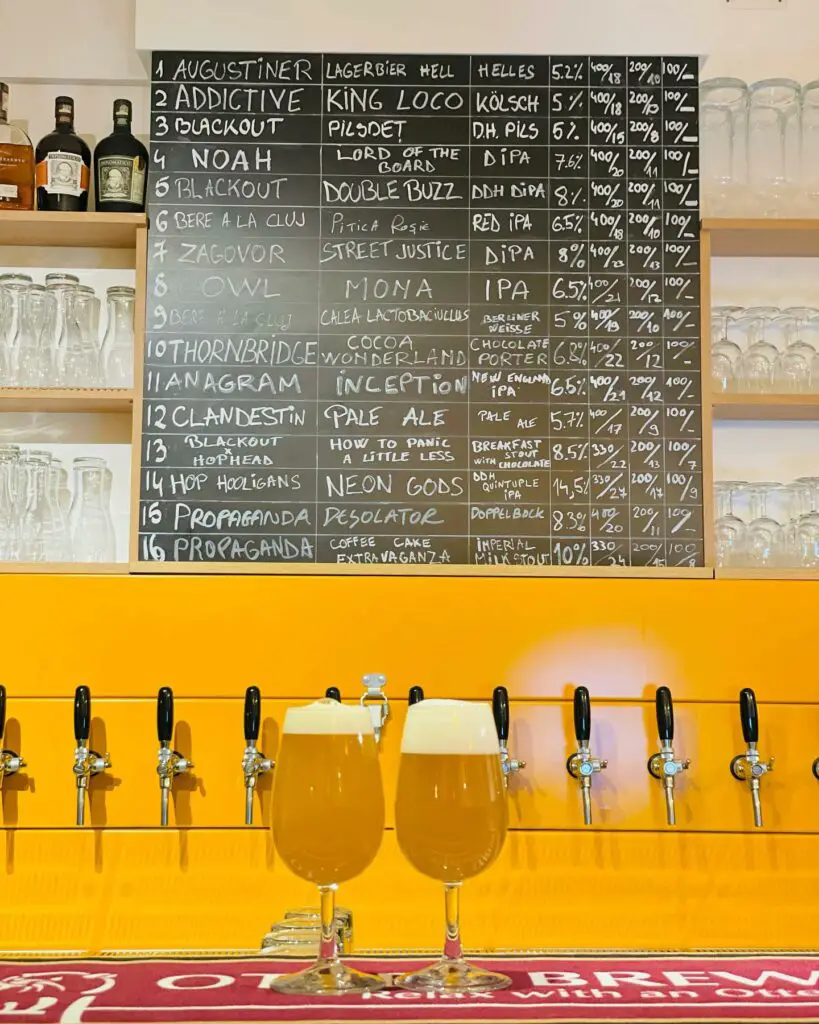 Two draft beers in front of a line of taps with yellow background.