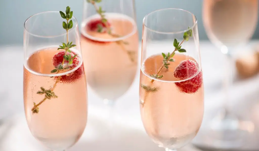 Three cocktail glasses with liquid, raspberries and thyme sprigs