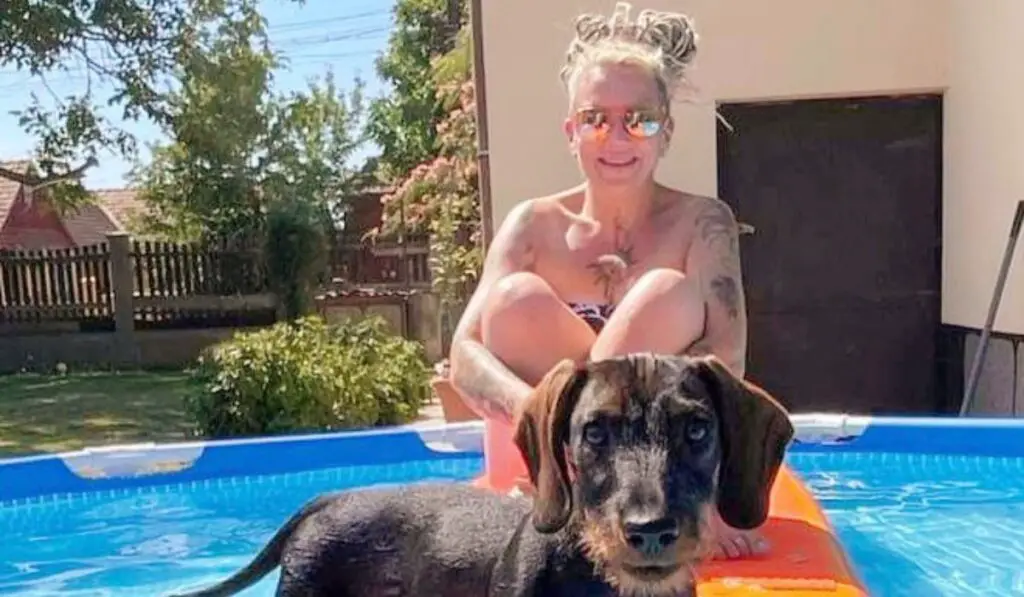 Woman and dachshund sitting on a paddle board in a pool.