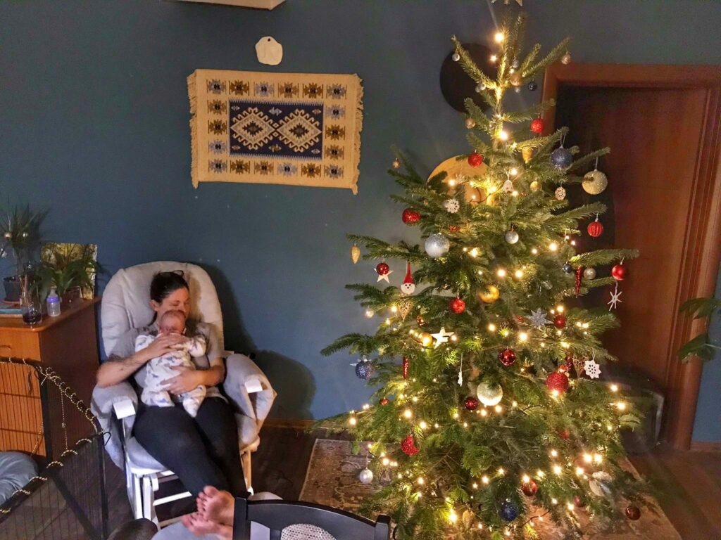 Decorated christmas tree in Romania next to a woman sitting with a baby.