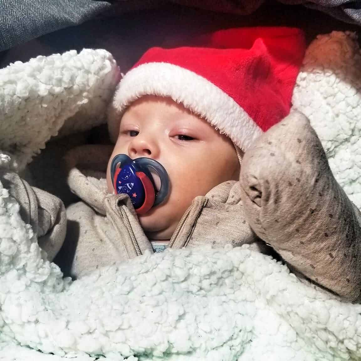 Baby in santa hat wrapped up at a Romanian Christmas gathering.
